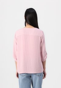 Lys rosa, teksturert bluse med trekvartermidler og rund hals, parret med lyseblå jeans. Enkelt design, ingen tilleggdetaljer.