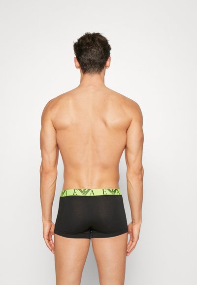 Boxers negros ajustados con una cinturilla de marca en verde lima. La tela parece suave con un diseño ajustado y longitud hasta mitad del muslo. Sin patrones visibles.