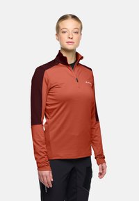 Langärmliges Hemd mit Viertelreißverschluss in rostorange mit dunkelbraunen Schulterakzenten. Hergestellt aus glattem Stretchmaterial, mit einem Logo auf der Vorderseite.