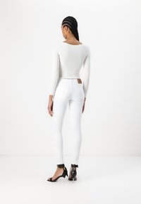 Λευκή ριμπ μπλούζα με μακριά μανίκια και στρογγυλή πλάτη, σε συνδυασμό με εφαρμοσμένο λευκό παντελόνι και μαύρες ψηλοτάκουνες σανδάλια με straps στον αστράγαλο.