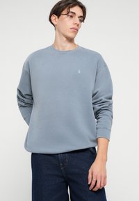 Light blue sweatshirt made of soft fabric, featuring a round neckline and ribbed cuffs, with a small logo embroidered on the chest.
