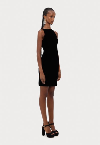 Robe sans manches en velours noir avec une coupe ajustée, longueur au genou, complétée par des talons plats noirs avec une bride de cheville.