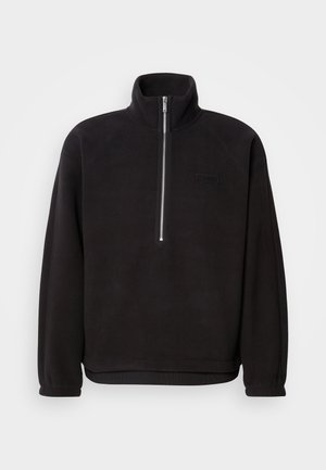 Svart fleece-pullover med høy hals og kvart glidelås, med elastiske mansjetter og en glat overflate. Diskret logomerke på brystet.