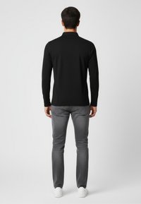 Czarna polo z długim rękawem i kołnierzykiem, zestawiona z szarymi jeansami i białymi trampkami. Prosty design, gładka faktura materiału.