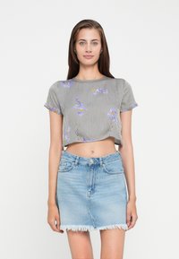 Top à rayures noir et blanc recoupé avec broderies florales, associé à une jupe en denim bleu clair avec un ourlet effiloché.