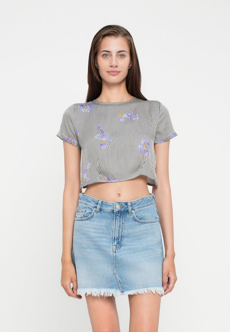 Top à rayures noir et blanc recoupé avec broderies florales, associé à une jupe en denim bleu clair avec un ourlet effiloché.