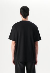 T-shirt noir à manches courtes avec une coupe décontractée, un col rond et une texture lisse. Sans motifs ni logos visibles.