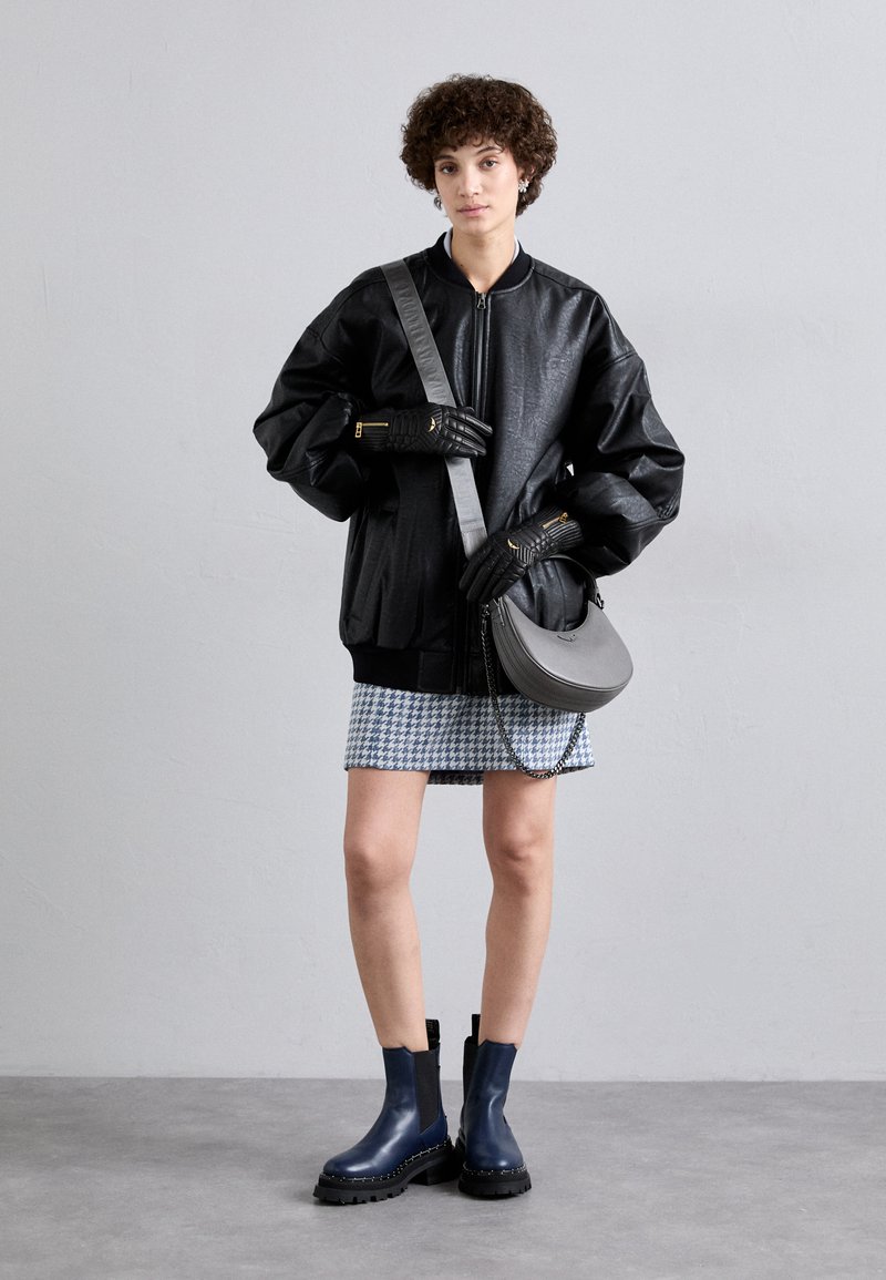 Black faux leather bomber jacket with oversized sleeves, checkered skirt, gray crossbody bag, and navy ankle boots with chunkier soles.