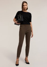 Zwarte geribbelde gebreide top met korte mouwen, bruine high-waisted broek met zijknopen, en zwarte high heels, accessorized met een zwarte tas.