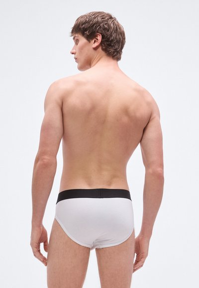 Calzoncillos blancos de algodón con una cintura elástica negra, mostrados desde atrás. El ajuste es ceñido, destacando una textura suave y un diseño simple.