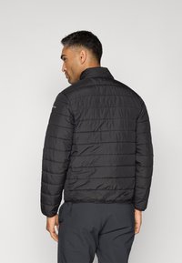 Veste matelassée noire avec un motif matelassé vertical et un col haut. Comprend des poches zippées et un ourlet ajustable. Texture de tissu lisse et brillante.