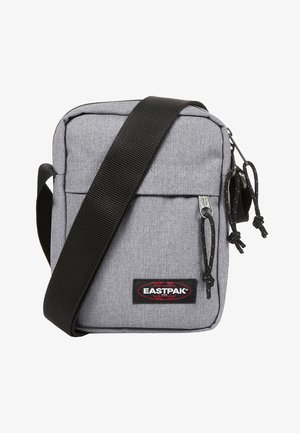 Szara torba na ramię z regulowanym czarnym paskiem, przednią kieszenią na zamek błyskawiczny i naszywką z logiem Eastpak. Teksturowany materiał i trwała konstrukcja.