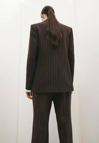 Traje marrón a rayas con una chaqueta entallada y pantalones a juego. Textura suave, silueta estructurada y cierre de un solo botón en la chaqueta.