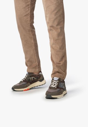 Zapatillas de camuflaje marrón con materiales de malla y ante, que presentan una suela blanca y negra, y detalles en naranja. Combinadas con pantalones de pana beige.