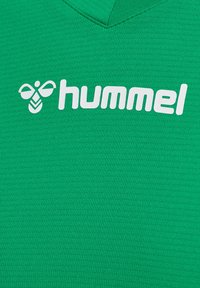 Grünes Sportshirt mit V-Ausschnitt-Design. Besteht aus einem strukturierten Stoff und verfügt über ein weißes Logo von "hummel" neben einem Bienen-Symbol.