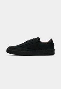 Melni zemi Reebok sporta apavi ar auklu aizdari, mīksts brūns iekšējais oderējums un diskrēta zīmola identifikācija uz sāniem un zoles, attēloti profilā.