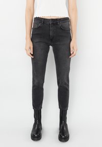 Černé skinny džíny ze strečového denimu s vybledlým povrchem, pěti kapsami a stříbrnými detaily. Kombinovány s černými kotníkovými botami.