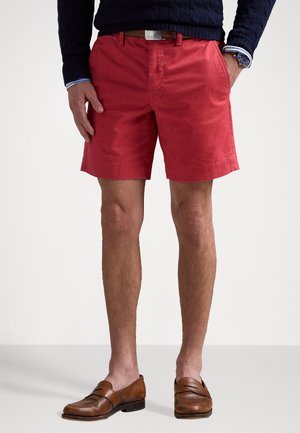 Shorts en coton rouges avec poches latérales, un devant plat et une taille avec une ceinture. Associés à des mocassins bruns.