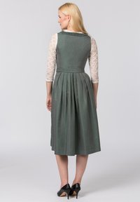 Grünes Kleid mit Falten, strukturiertem Oberteil und Häkelärmeln, kombiniert mit schwarzen High Heels. Die Rückansicht zeigt eine taillierte Silhouette.