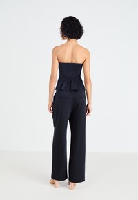 Tumes peplum-ülaosa ilma rihmadeta, millel on tekstuuriga kehake, koos laia jala pükste ja tagataskute ning nööbikasutusega.