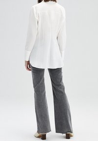 Witte lange mouwen shirt met een getailleerde pasvorm, met verticale naden. Geselecteerd met grijze wijde jeans en lichtgekleurde blokhak schoenen.