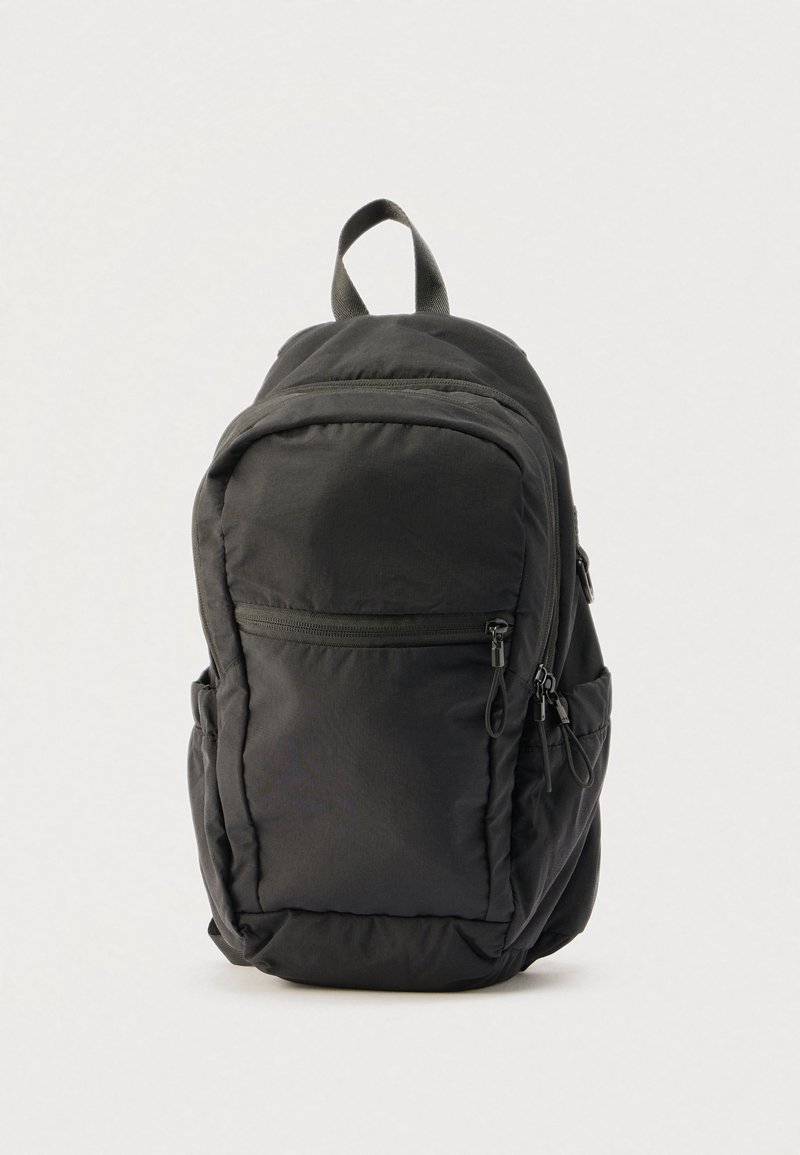 Sac à dos noir avec plusieurs compartiments zippés et une poignée supérieure, debout sur un fond clair uni.