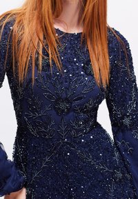 Námořnická modrá šaty s flitry a květinovou výšivkou z korálků. Dlouhé rukávy a kulatý výstřih, s propracovanými detaily a přiléhavou siluetou.