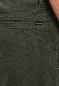 Grønne kordfløjlsstof med lodrette linjer, der har et Volcom-logo tag på lommen. Holdbar med en struktureret overflade og rigeligt syning.