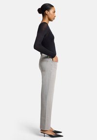 Black long-sleeve top, light gray straight-leg jeans, and pointed black heels. Model stands sideways with hands in pocket. Smooth texture.