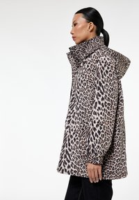 Luipaardprint jasje van zachte stof, met een hoge kraag, ingesnoerde mouwen en grote zakken. De dominante kleuren zijn beige, bruin en zwart.
