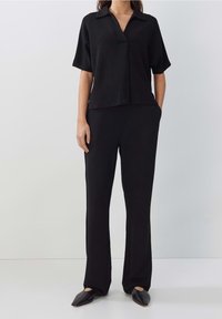 Černý top s krátkými rukávy a límečkem, doplněný o odpovídající kalhoty rovného střihu. Hladká tkanina s minimálním zdobením. Černé špičaté baleríny.