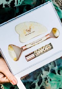 Zestaw narzędzi do pielęgnacji skóry, w tym różowo-złoty wałek jadeitowy, sercowy gua sha i szklana fiolka z kryształkami.