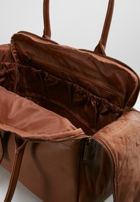 Borsa in pelle marrone con manici doppi, chiusura con zip e tasche interne. Finitura morbida e texturizzata con un compartimento spazioso foderato.
