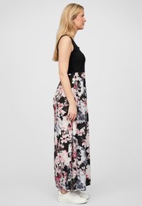 Robe maxi avec un corsage noir ajusté et une jupe fluide à fleurs dans des teintes de rose, blanc et noir, avec une texture lisse et longueur cheville.