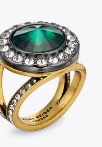 Bague en or ornée d'une grande pierre ovale verte, entourée de pierres claires. Design courbé avec des détails complexes sur le bandeau.