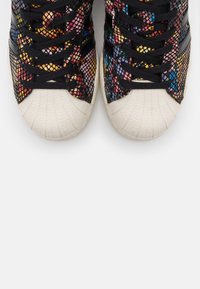 Gekleurde mesh sneakers met zwarte veters, voorzien van een gestructureerde witte rubberen neuskap en contrasterende zwarte strepen aan de zijkant.