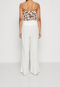 Bílé široké kalhoty s texturovaným povrchem v kombinaci s květinovým krátkým topem s tenkými ramínky, viditelnými na zádech.