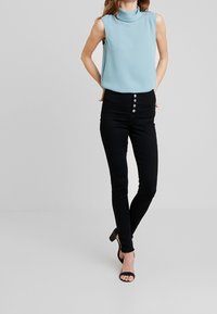 Ljusblå ärmlös topp med hög krage, tillsammans med högmidjade svarta skinny jeans med fem knappar, och svarta klacksandaler.