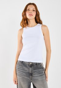 Hvit ribbestrikket tank topp med rund utringning, båret med falmet grå høytlivsjeans, som har en avslappet passform og lette teksturdetaljer.