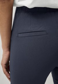 Pantaloni blu con una superficie liscia, dotati di una piccola tasca posteriore orizzontale e una cintura elastica.