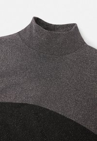 Gros plan sur un pull à col roulé gris charbon avec une subtile brillance et un panneau noir incurvé près de la poitrine.