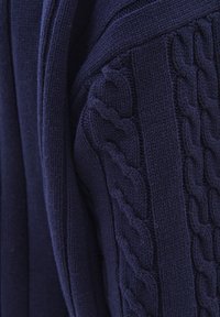 Suéter de punto azul marino que presenta un patrón de trenzado texturizado en un lado y un acabado liso en el otro, confeccionado en una tela suave de peso medio.
