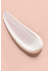 Cremiges, weißes Produkt in Tropfenform auf einem sanften rosa Hintergrund, mit einer glatten Textur und leichtem Glanz.