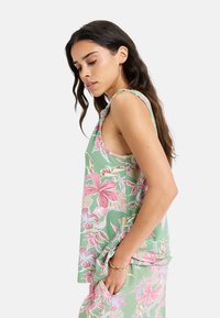 Floral tank top in pastel green with pink and white tropical patterns. Loose fit with shoulder tie detail and side pockets. Soft fabric texture.
