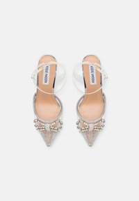 Talons slingback argentés avec des embellissements en perles et des pointes. Des sangles transparentes et une semelle intérieure beige complètent le design.