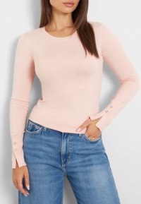 Vaaleanpunainen pitkähihainen paita pyöreällä kaula-aukkolla ja ribbineuloksella. Hihansuissa koristeelliset napit ja vartalonmyötäinen leikkaus.