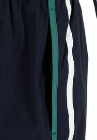 Pantaloni corti blu navy realizzati in un tessuto leggero e morbido. Presentano un accento verde laterale e una striscia verticale bianca. Vita regolabile con cordoncino.