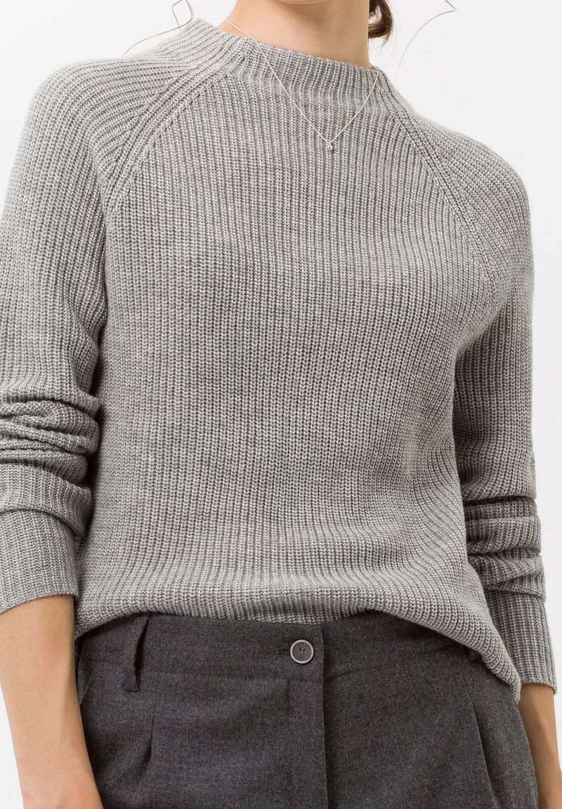 Pull en tricot gris avec une texture côtelée, un col arrondi et des manches raglan. Associé à un pantalon gris avec un détail de boutons.