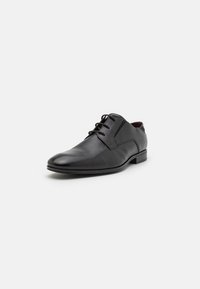 Zapato de vestir de cuero negro con un diseño elegante, punta redondeada y textura suave. Presenta cordones y un tacón bajo apilado.