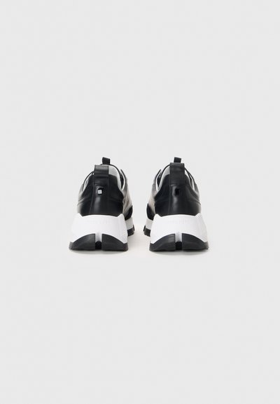 Zapatillas deportivas en blanco y negro con una parte superior de cuero suave, suela de goma gruesa y acentos texturizados distintivos en el talón.